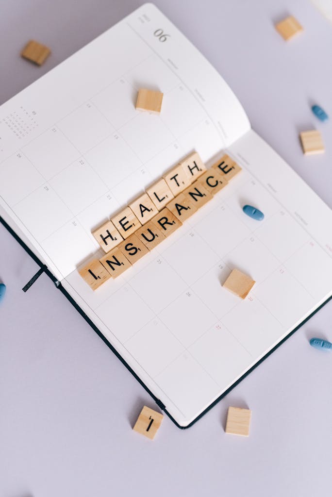 Flat lay of planner with 'Health Insurance' in Scrabble tiles, emphasizing planning and health.