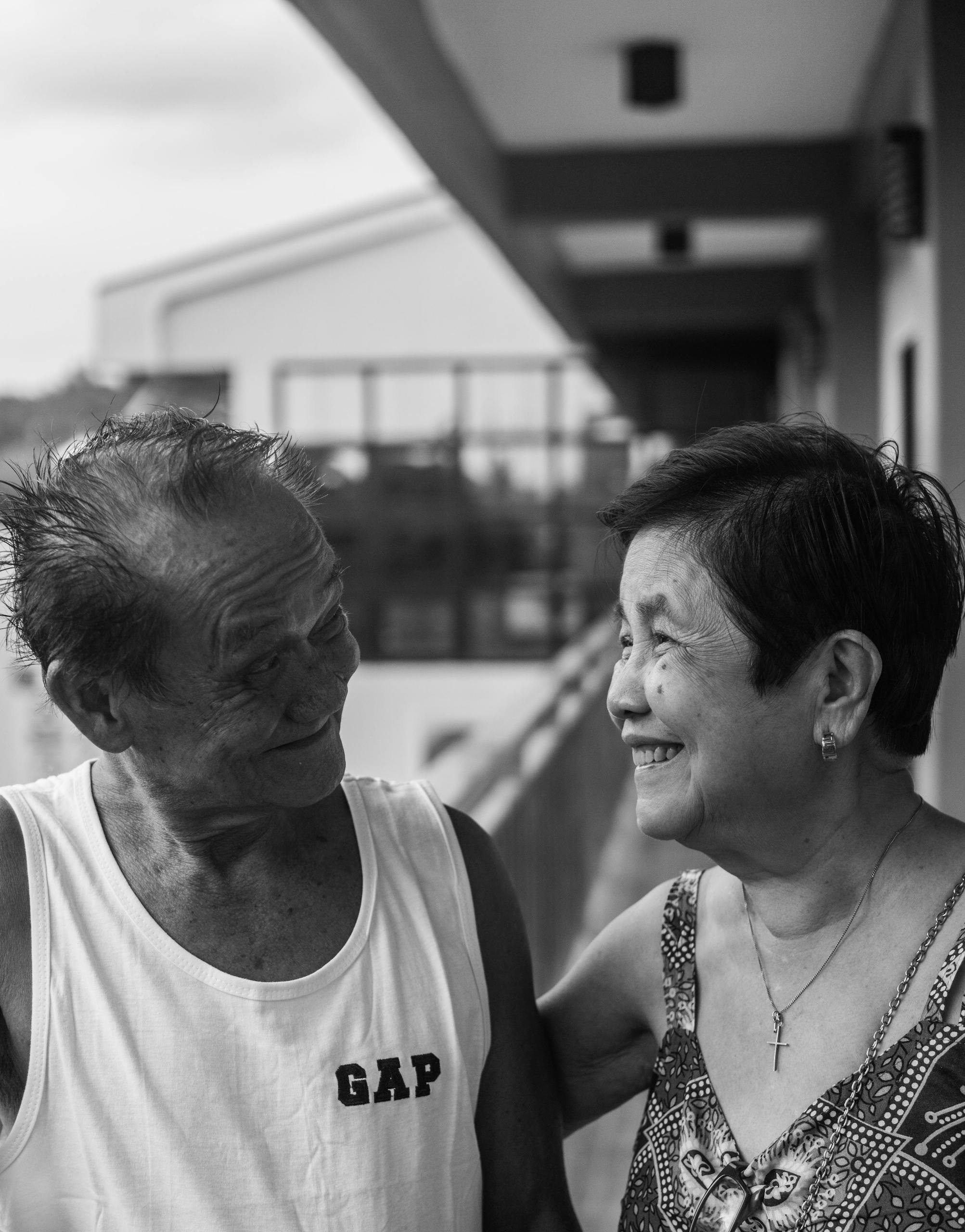 A black and white portrait of a smiling elderly couple sharing a joyful moment outdoors.