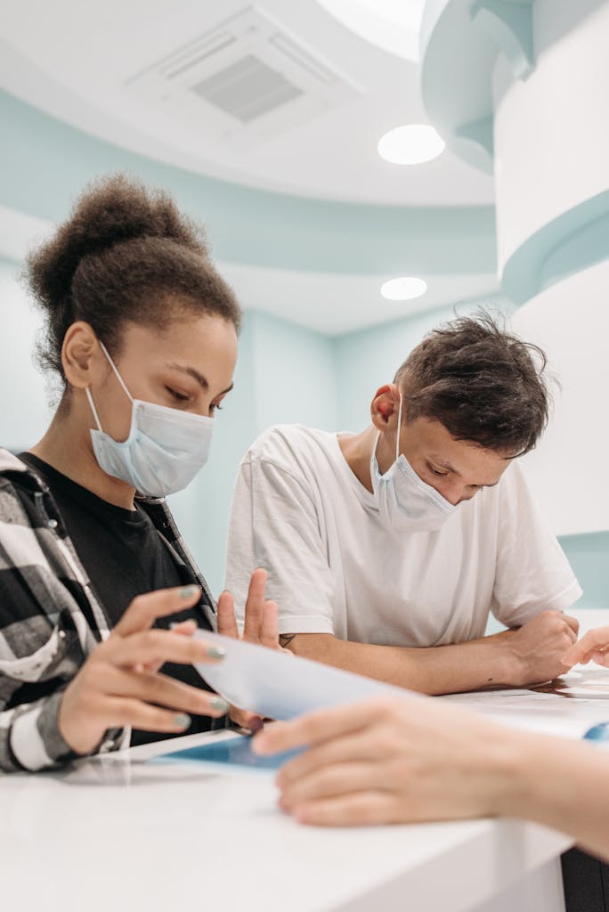 A couple wearing face masks reads documents at a clinic reception, emphasizing healthcare and safety.