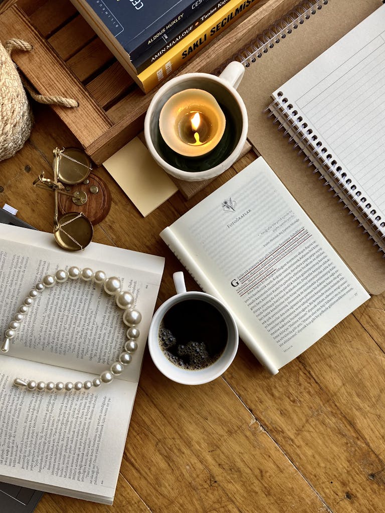 A warm flat lay featuring books, candle, coffee, and pearl necklace for a cozy vibe.