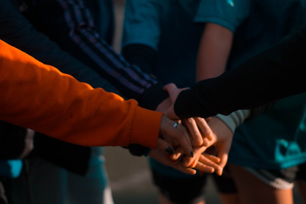 A close-up of diverse hands stacked together outdoors, symbolizing teamwork and unity.