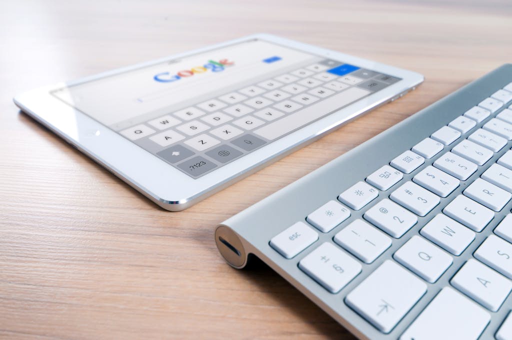 A modern tablet displaying a search engine logo next to a wireless keyboard on a wooden desk.