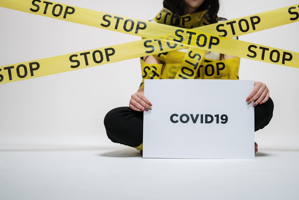 A woman holding a COVID-19 sign surrounded by yellow stop tape, conveying caution and awareness.