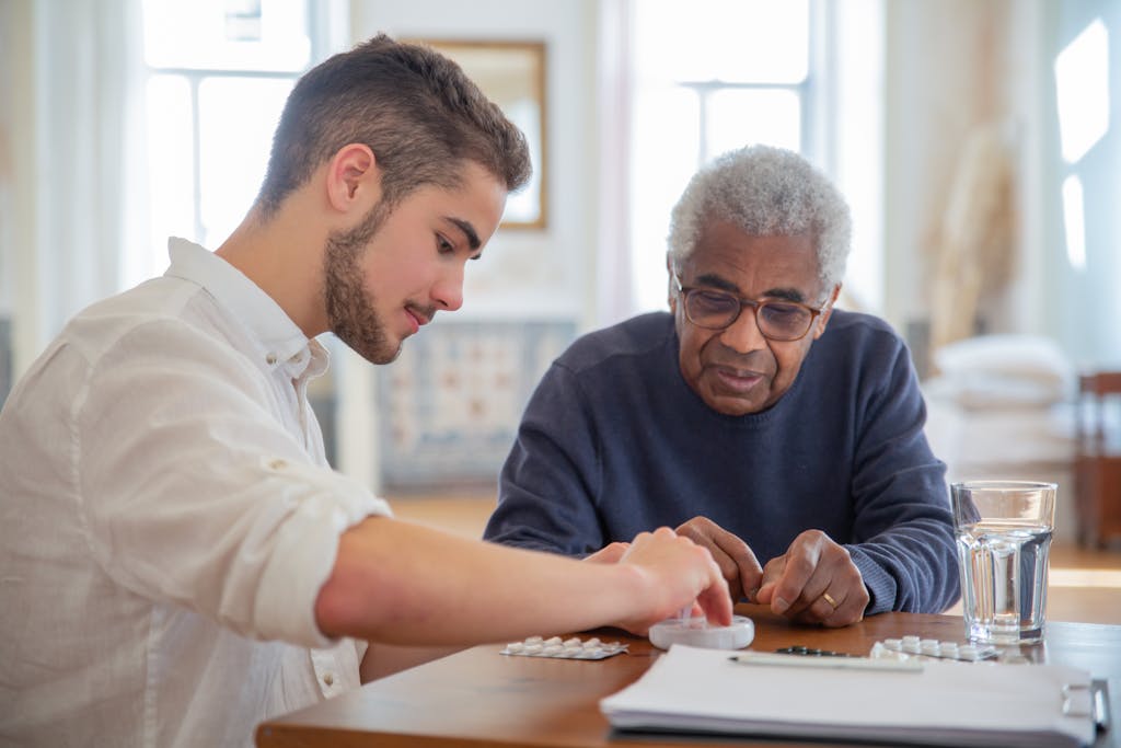 A young volunteer helps an elderly man manage his medication at a nursing home.