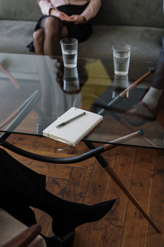 Close-up of a counseling session with two glasses of water and a notepad on a glass table.