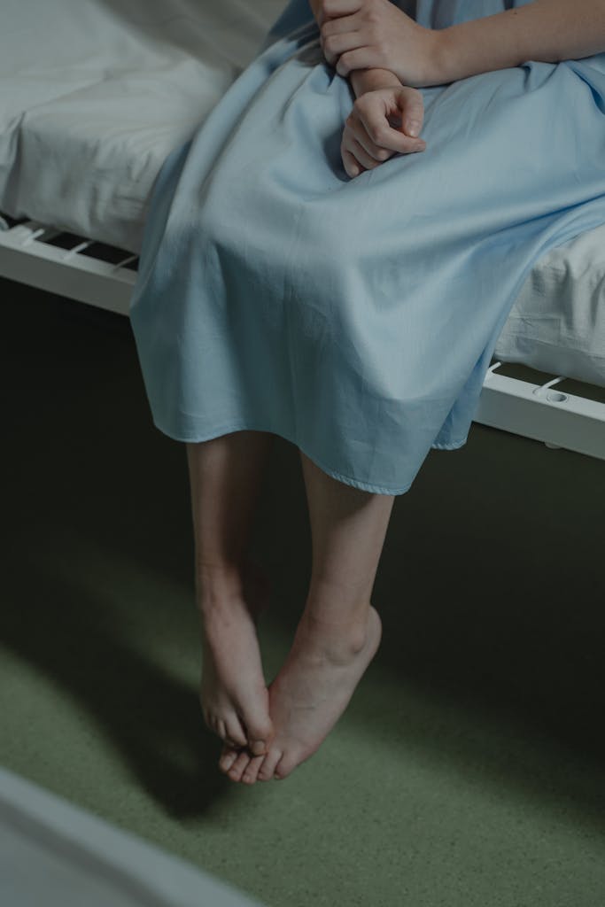 Close-up of a person sitting on a hospital bed with a thoughtful posture. Indoor lighting.