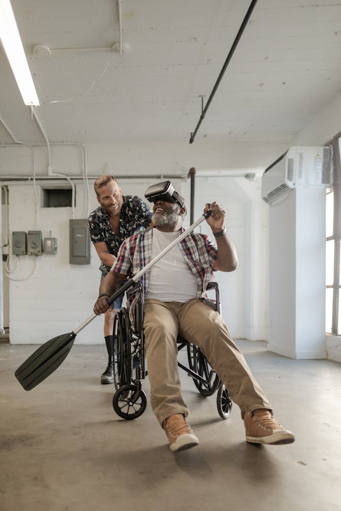 Man in wheelchair using VR headset for rehabilitation, assisted by friend.