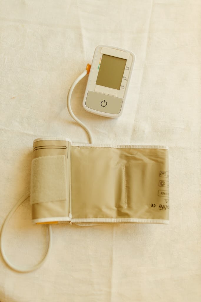 Top view of a digital blood pressure monitor and cuff on white fabric background.